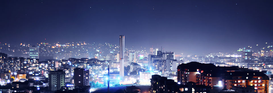 Nattbilde av en by med belyste bygninger og en stjernetetthimmel.
