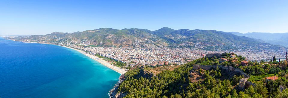 Panoramabilde av Antalya med klarblått hav på den ene siden og grønne fjell på den andre.