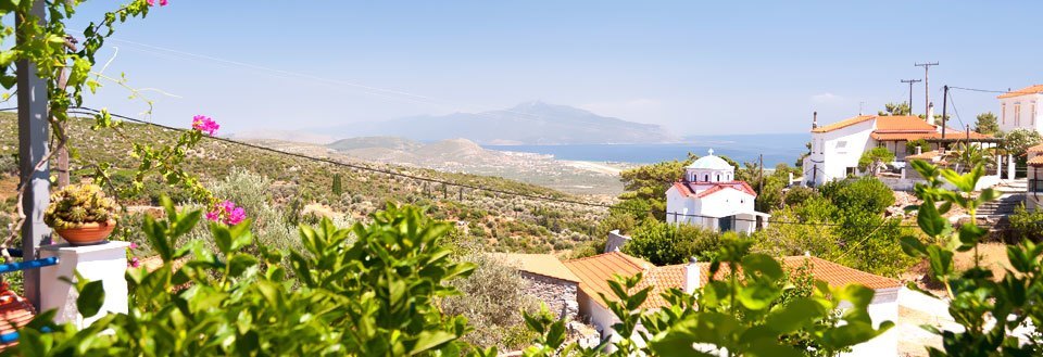 En idyllisk landsby med hvite hus på Samos, grøntområder og en kirke, med fjell i bakgrunnen.