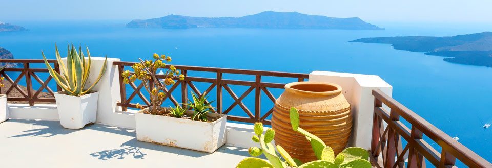 Terrasse med utsikt over sjøen og planter i potter. Klart blått vann og himmel.