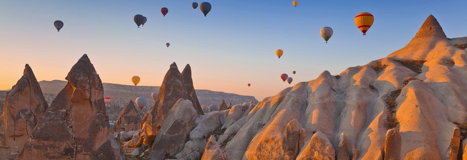 Fargerike varmluftsballonger som svever over et unikt steinlandskap i solnedgangen.