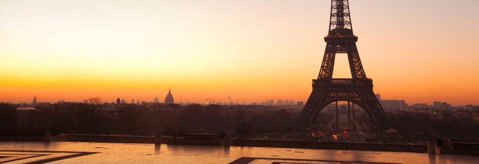 Solnedgangen bak Eiffeltårnet i Paris viser en varm oransje himmel og byens silhuett.