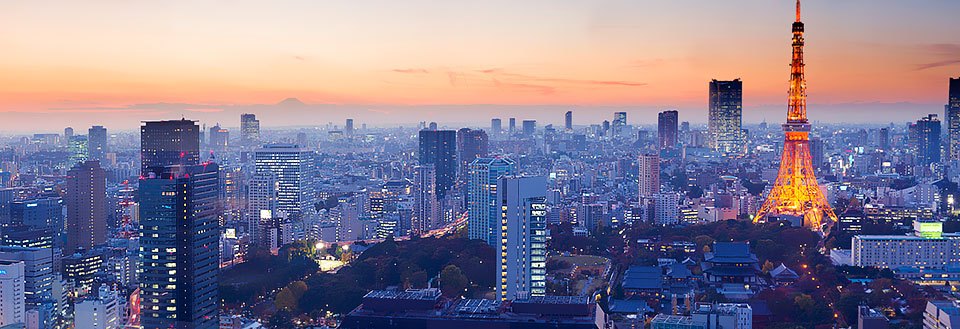 Skumring over Tokyo med høyhus og et fremtredende, opplyst tårn i forgrunnen.