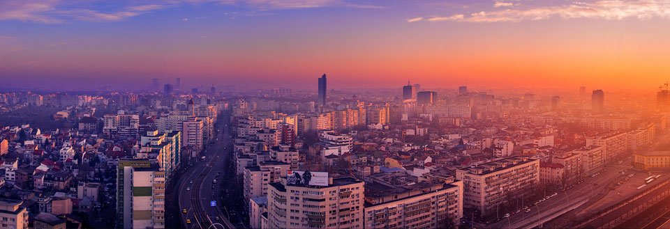 Bilde av Bukarest  i solnedgang med skyskrapere og en travel hovedvei.