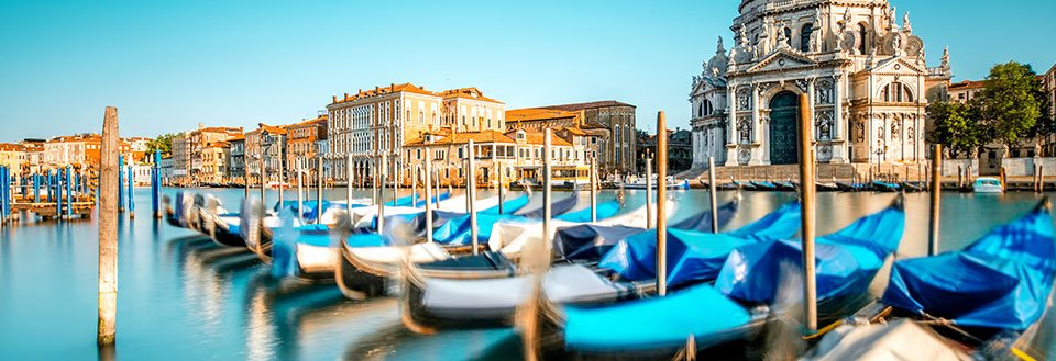 Bildet viser gondoler som flyter på stille vann i Venezia, omgitt av historiske bygninger.