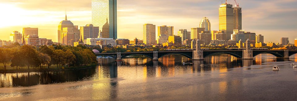 Bildet fremviser Boston ved solnedgang med skyskrapere, en bro, og speilinger i vannet.