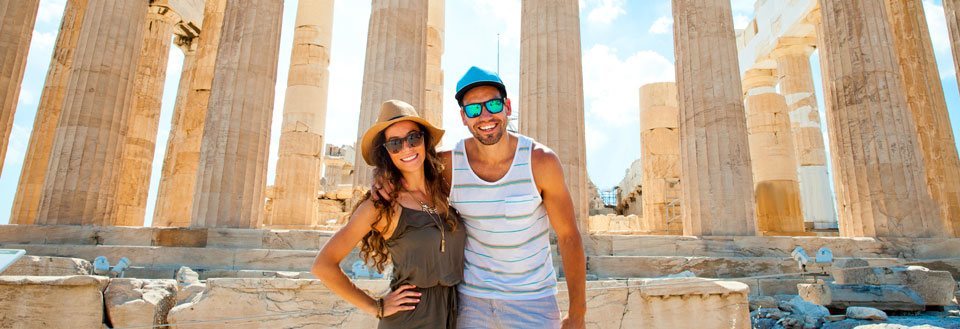 To glade mennesker poserer foran de majestetiske søylene i Parthenon på Akropolis.