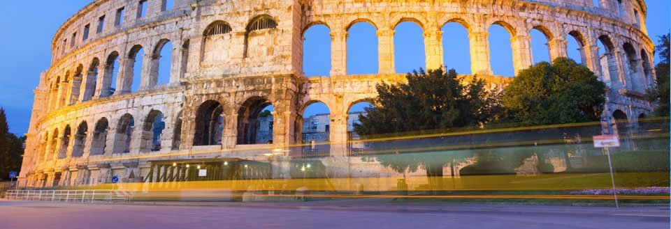 Kveldsbilde av det antikke Colosseum i Roma med lang eksponeringstid som viser lysstriper fra kjøretøy.