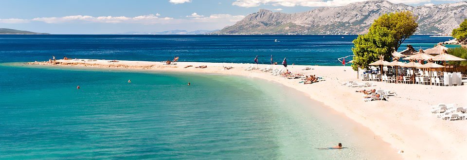 Et fredelig strandlandskap med krystallklart hav, hvit sand og fjell i det fjerne.