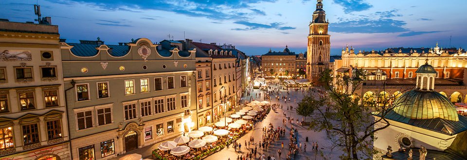 En travel torg i Krakow i skumringen med historiske bygg, folkemengder og utendørs kafeer.