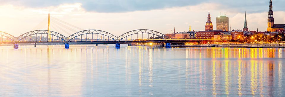 Bilde av Riga ved elven i skumring med lys som reflekteres i vannet og en bro i bakgrunnen.