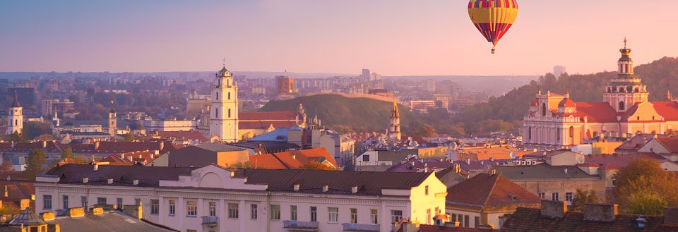 Vilnius i solnedgangen, med kirker, gamle bygninger og en varmluftsballong i luften.