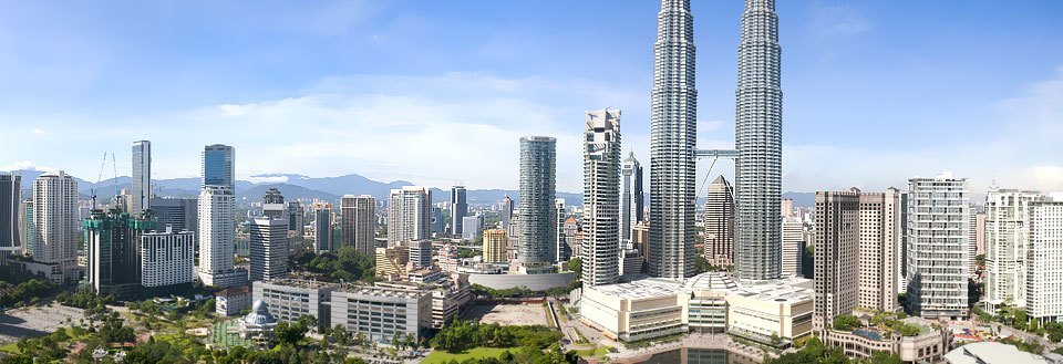 Kuala Lumpur med Petronas Towers, ulike bygninger og grøntområder. Klar blå himmel bak.