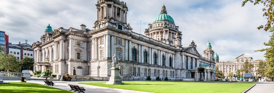 Belfast rådhus i Nord-Irland. Bygget er en imponerende struktur med flere kuppel og tårn, alle i barokk stil, med en slående grønn kobberkuppel i sentrum. Foran rådhuset ligger en velholdt gressplen, omringet av gangveier og benker