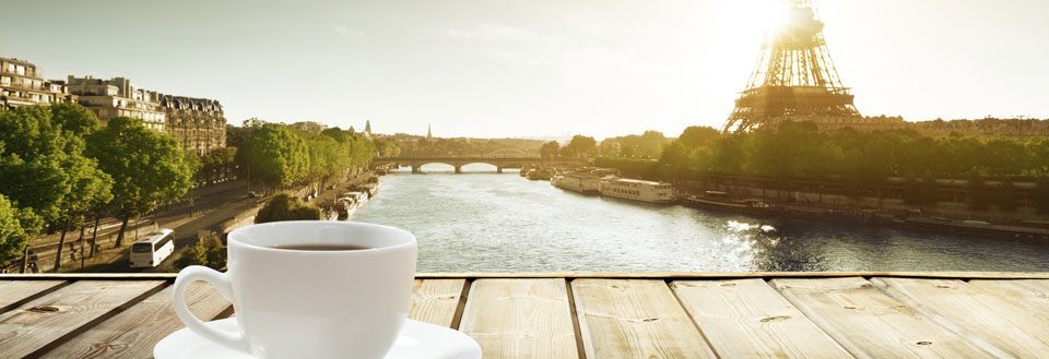 En hvit kaffekopp på et trebord med utsikt over Seinen og Eiffeltårnet i Paris.