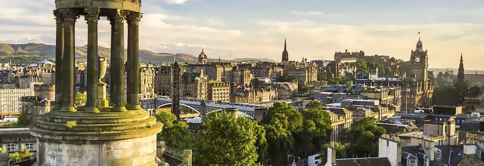 View over Edinburgh med klassiske bygninger, monumenter og grøntområder under en klar himmel.