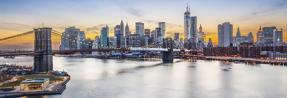 Panoramabilde av New York i skumringen med en berømt bro og lysende skyskrapere.