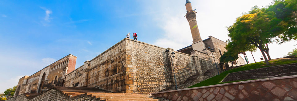 Historisk bygning med en minaret, høye steinvegger og folk som nyter utsikten.