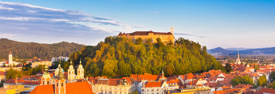 Europeisk by i solnedgang, med historiske bygninger og et slott på en høyde.