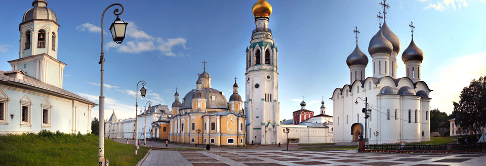 Panoramabilde av et russisk kirkekompleks med fargerike kupler og tårn under en klar himmel.