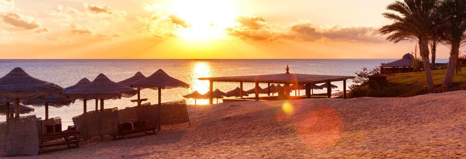 Solnedgang på stranden med stråparasoller og solsenger som vender mot havet.