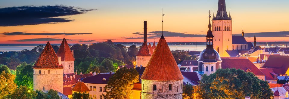 Solnedgang bak en historisk by med spir og tårn mot en fargerik himmel.