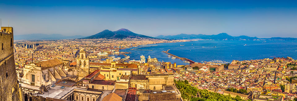 Panoramautsikt over en travel by med historiske byggverk og en berømt vulkan i bakgrunnen.